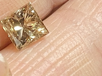 指先に乗せたスクエアシェイプのコニャックダイヤモンドの接写