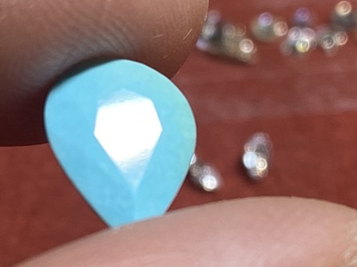 指先で持った、ペアシェイプカットの澄んだトルコ石