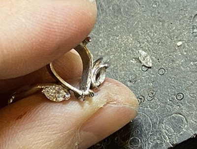 白い布の上でプラチナ製のリング枠が完成、脇石のダイヤモンドをセット中。