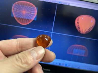 琥珀を手に持ち、画面上の3D設計と見比べている写真