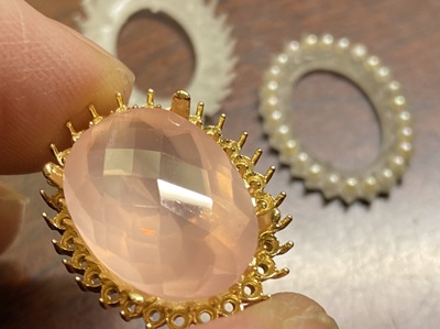 指先で持たれたK18金製のペンダント枠に、ローズクォーツを載せてサイズを確認している様子。