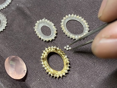 ピンセットで直径2ミリほどの極小ベビーパールを1粒ずつ掴み、金枠の台座にセットしていく細かな作業風景。