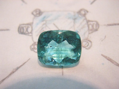 クッションカットのパライバトルマリン原石、手描きデザインスケッチの上に置かれた鮮やかなブルーグリーンの宝石