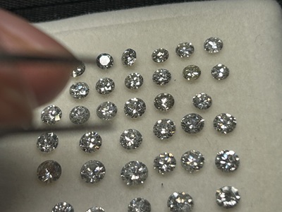トレイに整列した多数のラウンドブリリアントカットダイヤモンド、ピンセットで1石つまんでいる様子