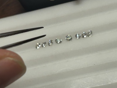 ピンセットでつまんだグラデーションに並ぶ小粒ダイヤモンド7石、サイズ確認の様子