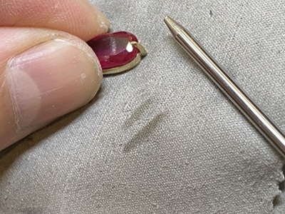 赤い石をペンダント枠に合わせて石留め前確認している工程