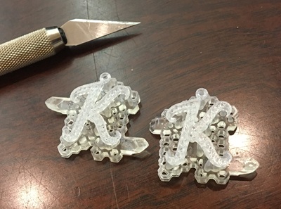 木製テーブルの上に置かれた、サポート材付きの2つの樹脂製「K」原型とデザインカッター。