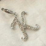 白いクッションの上に置かれた、完成品のイニシャル「K」ペンダント。全体がキラキラと輝いている。