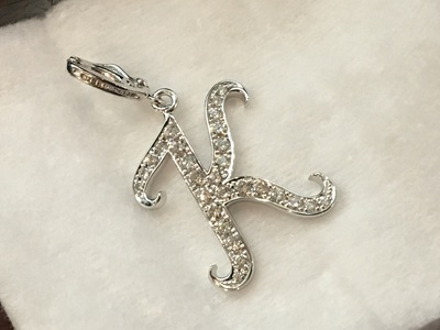 白いクッションの上に置かれた、完成品のイニシャル「K」ペンダント。全体がキラキラと輝いている。