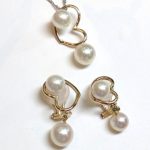 白い背景に並べられた、お揃いの蝶デザインの真珠イヤリングとペンダントのセット。