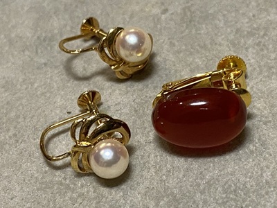 オーバル型のレッドアンバー（赤琥珀）がセットされたゴールドのイヤリング（片方）と、小粒の真珠がセットされたイヤリング。
