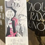 「宇野亜喜良展」の縦型の案内チラシ。背景には展覧会のポスターが写っている。