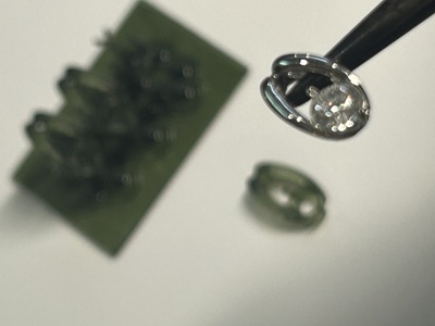 新しいプラチナ製の台座の中央にダイヤモンドをセットし、これから石留めを始める直前の精密な手元の写真