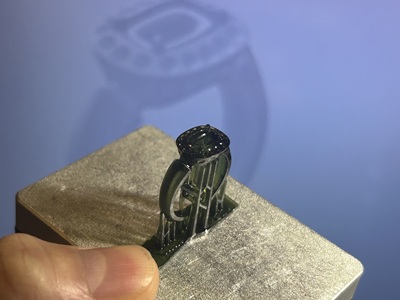 3Dプリンターの金属プラットフォームの上に、緑色の半透明レジンで立体出力された指輪原型のマクロ写真