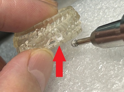 拡大された樹脂原型の石留め部分（シャトン）に、ダイヤバー（リューターポイント）を当てて精密に微調整を行っている手元の写真