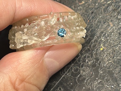 半透明の樹脂原型の5本爪の中央に、選ばれた一番輝きの強いブルーダイヤモンドを仮置きして石合わせをしているマクロ写真