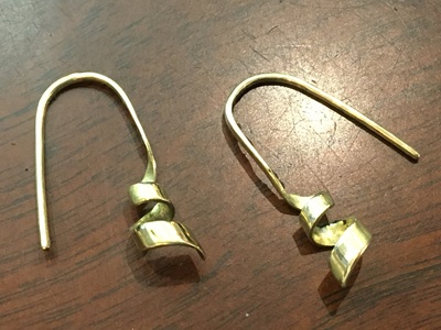 木目の作業台の上に並べられた、左右の曲がり具合やフックのバランスを均等に整える前の、金製のピアス本体パーツ