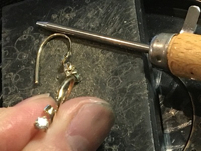 金製のリボンピアスの先端部分に、別パーツで作られたダイヤモンド用の小さな爪付き石座（シャトン）を仮あわせしている作業風景