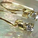 虹色に輝く貝殻のトレイの上に美しく飾られた、18金ゴールドのらせんリボンの先端でダイヤモンドがまばゆくシンチレーションを放っている完成ピアス