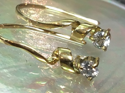 虹色に輝く貝殻のトレイの上に美しく飾られた、18金ゴールドのらせんリボンの先端でダイヤモンドがまばゆくシンチレーションを放っている完成ピアス