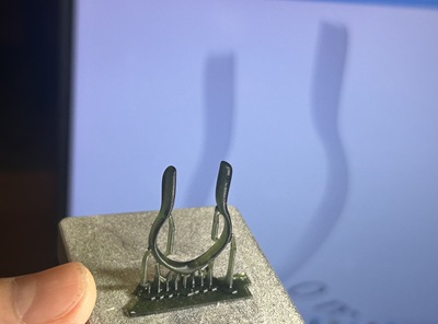 3Dプリンターから出力された直後の、サポート材がついた黒い樹脂製のリングモデル。