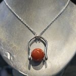 ネックレスチェーンに通されたシルバーカラーのリング。中央にオレンジ色の珊瑚がセットされている。