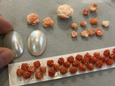 トレイの上に並べられた、繊細な薔薇の彫刻（カービング）が施されたピンクや赤の様々な珊瑚。