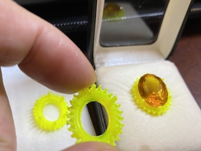 3Dプリンターで出力されたグレーの樹脂製ペンダント枠の原形に、シトリントパーズを仮あわせしている様子。