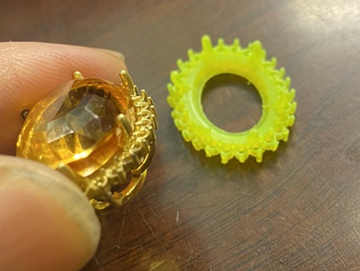 作業机の上で、工具を用いてK18ペンダント枠の内側を整え、シトリントパーズの厚みに合わせて調整する職人の手元。