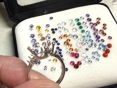 リング枠の隣に、両サイドへ配置するさまざまな色味のカラーストーン（ルース）を並べて吟味している様子