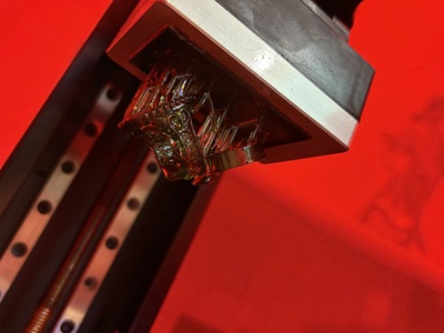 赤い光に包まれた光造形3Dプリンターの内部で、緑色の透明な樹脂で作られた複雑なデザインの指輪が造形されている様子。