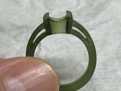 緑色の透明な樹脂で作られた指輪原型の別アングル。人差し指と親指で支えられ、指輪の円形の断面と、石座の側面がはっきりと見える。