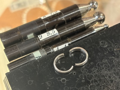黒い台の上に並べられた、綺麗に形が整った一対のフープ型のプラチナピアスパーツと、奥に見える3本の芯棒。