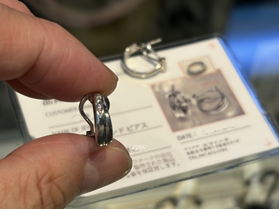 指先で持った完成済みのプラチナメレダイヤピアスと、その背景に写るラミネート加工されたカード型のリメイク証明書。