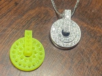 木目のテーブルの上に置かれた、最初の緑色の樹脂原型と、最終チェックおよびバフ磨きを終えてプラチナチェーンが通された完成品ペンダントの画像。