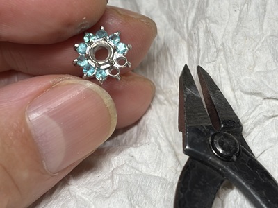 ヤットコなどの工具を用いて、プラチナ枠の周囲に色鮮やかなパライバトルマリンを共有爪で固定している手元