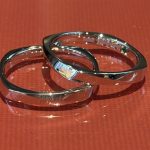 赤い背景の上に置かれ、内側の刻印とエメラルドやダイヤモンドのシークレットストーンが輝く2本の結婚指輪