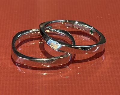 赤い背景の上に置かれ、内側の刻印とエメラルドやダイヤモンドのシークレットストーンが輝く2本の結婚指輪