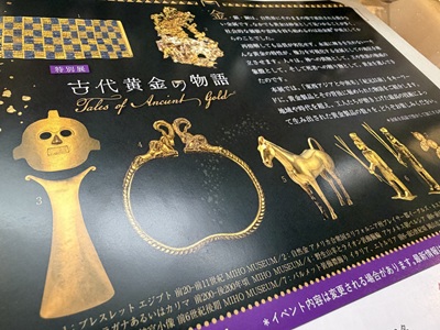 チラシ裏面の古代黄金製品のクローズアップ。太陽の仮面と胸飾りが目立つ