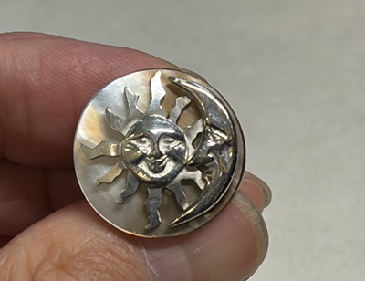 完成したSun & Moonブローチを指で持っている様子。虹色のシェルが美しい。